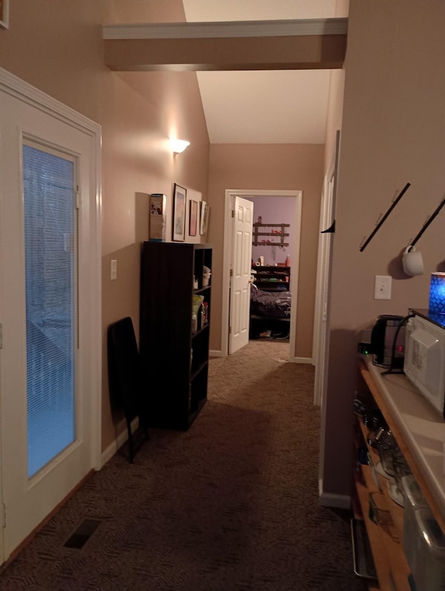 hall featuring lofted ceiling, visible vents, dark carpet, and baseboards