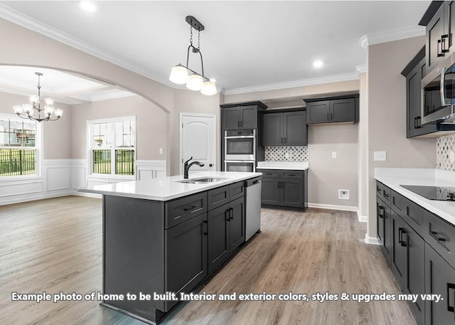 kitchen with arched walkways, light wood-style flooring, stainless steel appliances, light countertops, and a sink