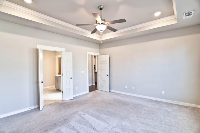 unfurnished bedroom featuring carpet floors, visible vents, baseboards, a raised ceiling, and crown molding