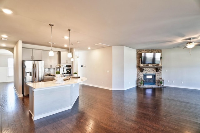 kitchen featuring stainless steel appliances, dark wood-type flooring, a fireplace, light countertops, and an island with sink