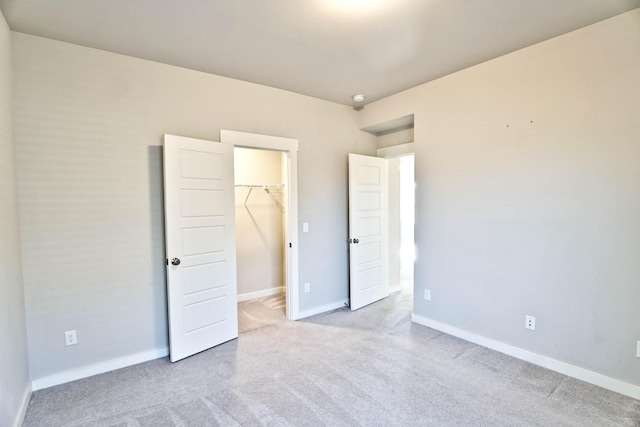 unfurnished bedroom with a walk in closet, light colored carpet, and baseboards