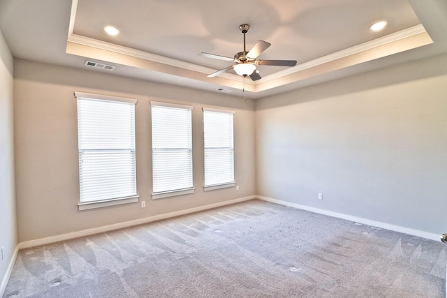 carpeted spare room featuring a tray ceiling, visible vents, crown molding, and baseboards