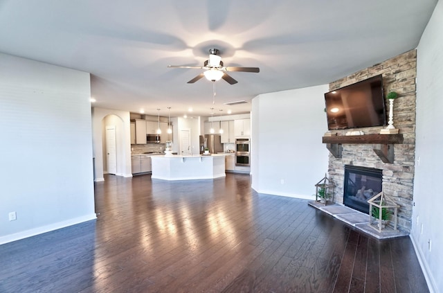 unfurnished living room featuring dark wood finished floors, a sink, a stone fireplace, ceiling fan, and baseboards