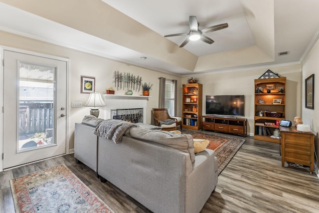 living room featuring dark wood-style flooring, a raised ceiling, visible vents, a healthy amount of sunlight, and a lit fireplace