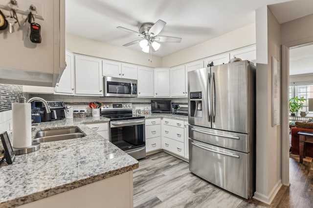 kitchen featuring stainless steel appliances, decorative backsplash, white cabinets, a sink, and light wood-type flooring