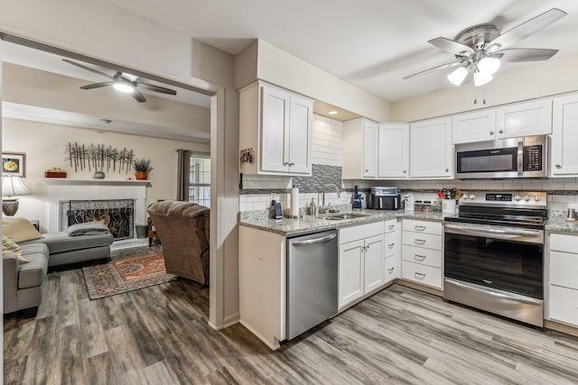 kitchen featuring appliances with stainless steel finishes, open floor plan, wood finished floors, a lit fireplace, and a sink