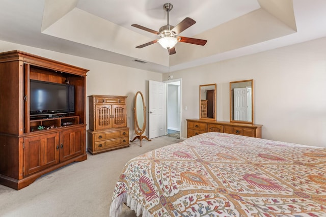 bedroom with a ceiling fan, a raised ceiling, visible vents, and light carpet