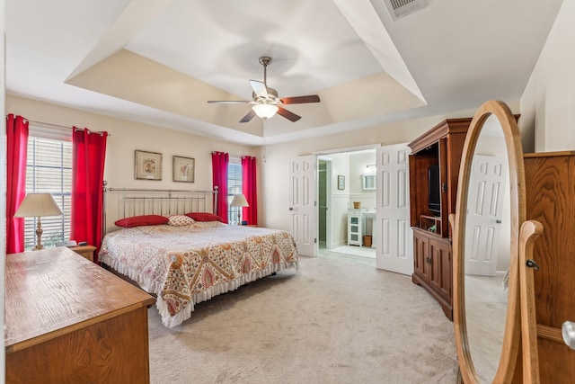 bedroom featuring visible vents, a raised ceiling, a ceiling fan, light colored carpet, and ensuite bathroom