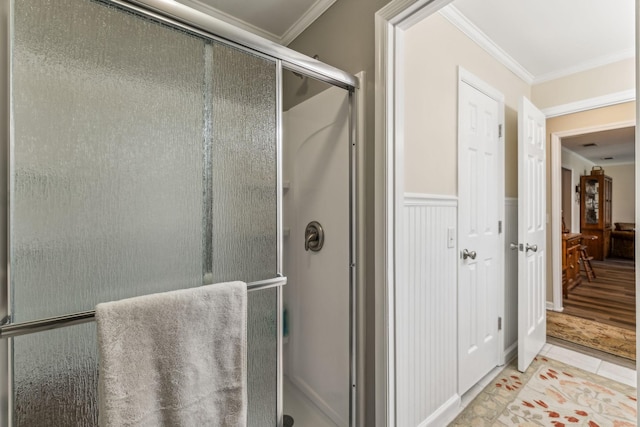 bathroom with a wainscoted wall, a stall shower, tile patterned flooring, and crown molding