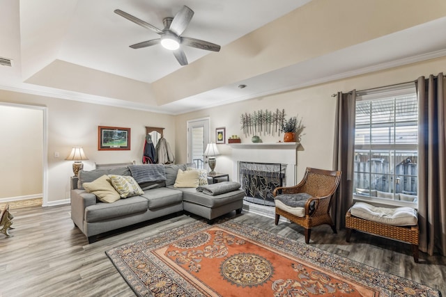 living area featuring ceiling fan, a fireplace, wood finished floors, visible vents, and a tray ceiling