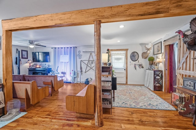 living area featuring ceiling fan, recessed lighting, wood finished floors, a wall mounted AC, and beam ceiling