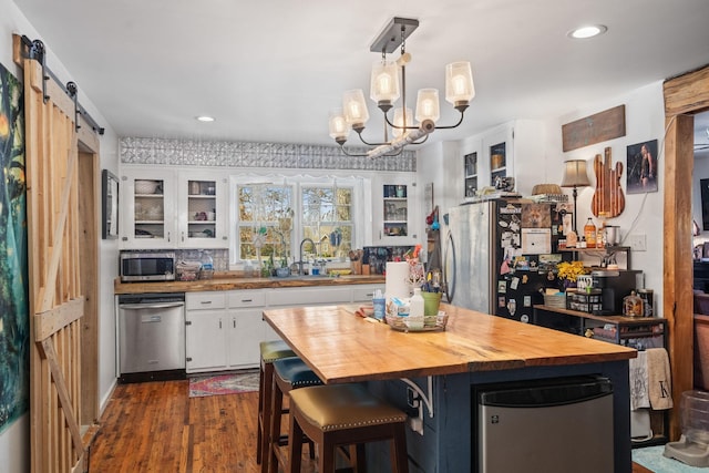 kitchen featuring a barn door, appliances with stainless steel finishes, white cabinets, a sink, and butcher block countertops