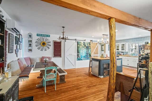 living room with a chandelier, a barn door, wood finished floors, an AC wall unit, and beamed ceiling