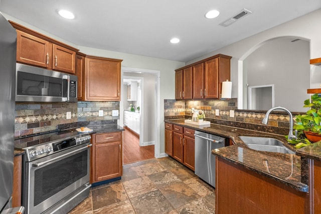 kitchen featuring stainless steel appliances, a sink, visible vents, backsplash, and dark stone countertops