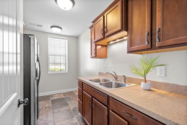 kitchen featuring visible vents, fridge with ice dispenser, light countertops, stone tile flooring, and a sink