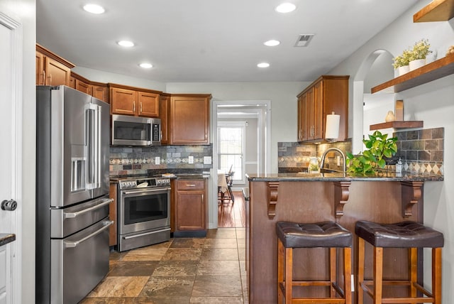 kitchen with visible vents, brown cabinetry, a breakfast bar area, a peninsula, and stainless steel appliances