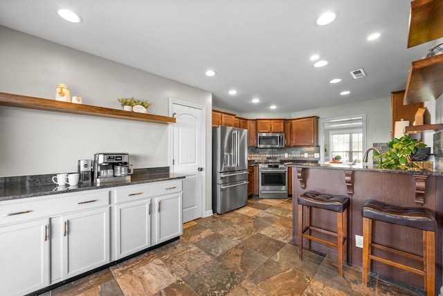 kitchen with open shelves, appliances with stainless steel finishes, visible vents, and a kitchen breakfast bar