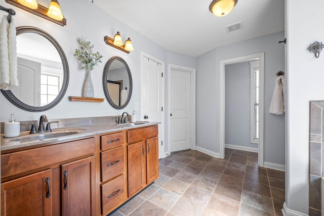 bathroom with double vanity, baseboards, visible vents, and a sink