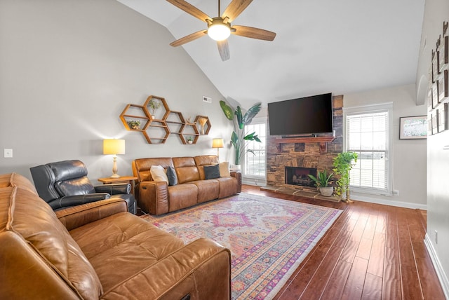 living area with hardwood / wood-style floors, high vaulted ceiling, a wealth of natural light, and a stone fireplace