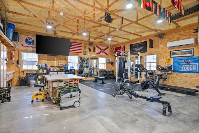 gym featuring a wall unit AC, a healthy amount of sunlight, a high ceiling, and a workshop area