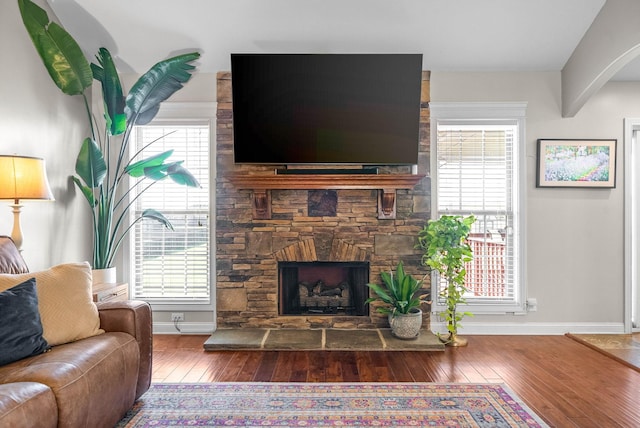 living area featuring plenty of natural light, a stone fireplace, and hardwood / wood-style flooring