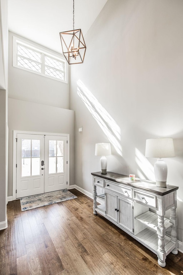 foyer entrance featuring dark wood-type flooring, an inviting chandelier, a towering ceiling, and baseboards