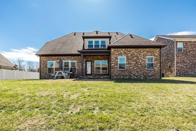 back of house with a shingled roof, fence, a lawn, and brick siding