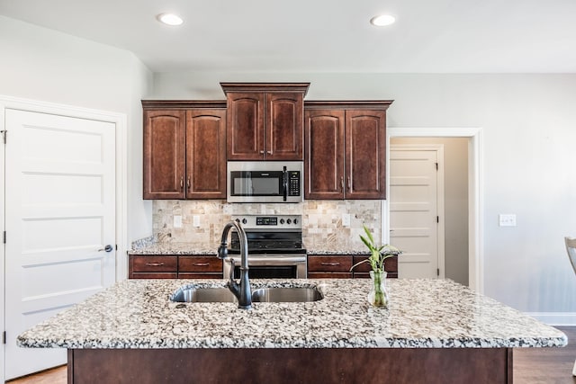 kitchen with stainless steel appliances, dark brown cabinets, decorative backsplash, and light stone countertops