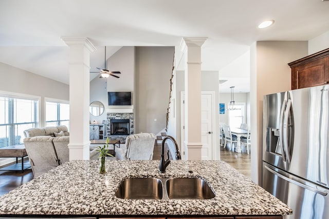 kitchen with stainless steel fridge, decorative columns, a sink, and a stone fireplace