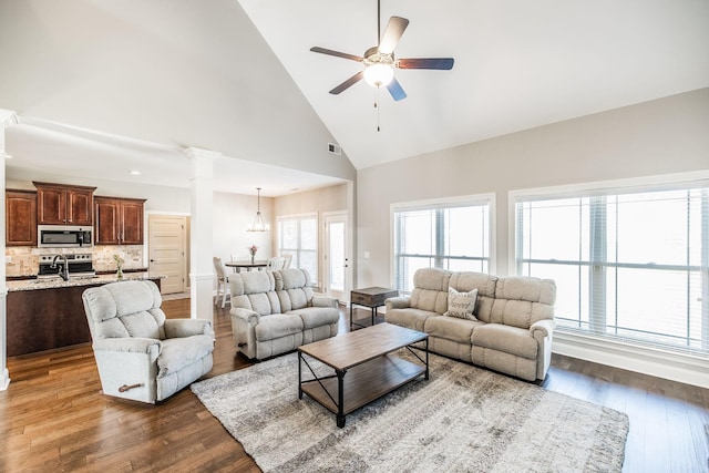 living room featuring visible vents, a ceiling fan, dark wood-style flooring, ornate columns, and high vaulted ceiling