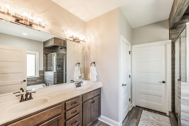 bathroom featuring double vanity, a shower stall, a sink, and wood finished floors