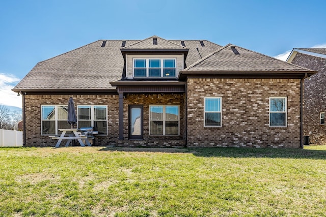 back of property featuring brick siding, roof with shingles, fence, and a yard