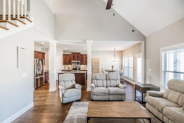 living area with dark wood-style flooring, ornate columns, visible vents, high vaulted ceiling, and baseboards