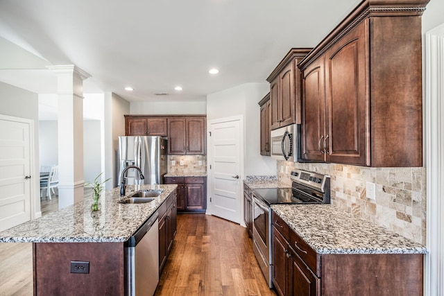 kitchen featuring decorative columns, light stone counters, dark wood-style flooring, stainless steel appliances, and a sink