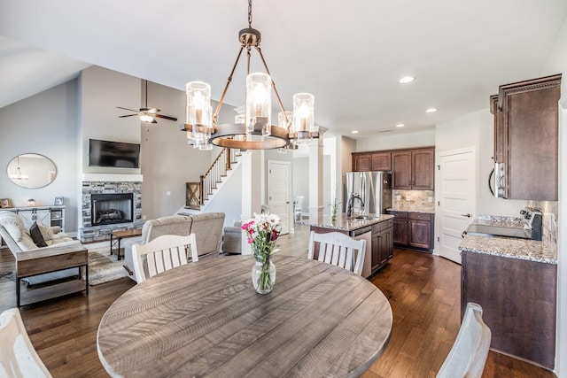 dining space with dark wood finished floors, recessed lighting, stairway, vaulted ceiling, and a stone fireplace