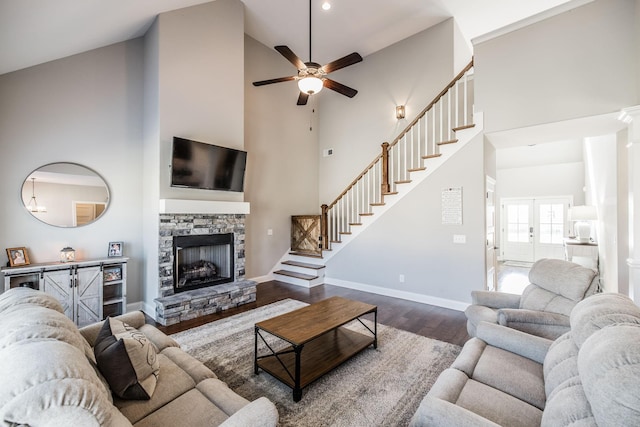 living area featuring a stone fireplace, dark wood-type flooring, a towering ceiling, and baseboards