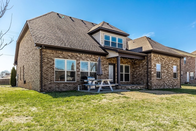 rear view of property with a yard, brick siding, roof with shingles, and a patio area