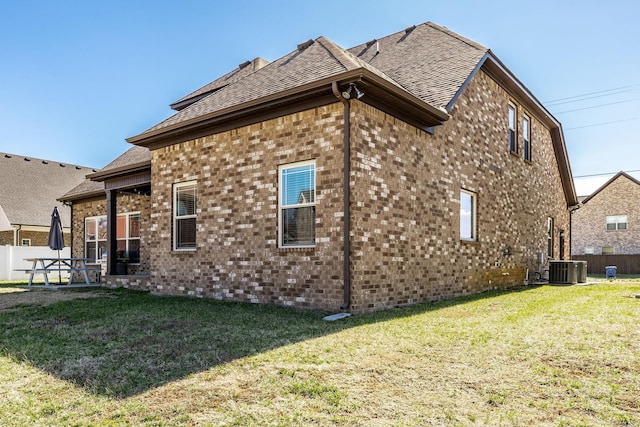 rear view of property with central AC, brick siding, a lawn, and fence