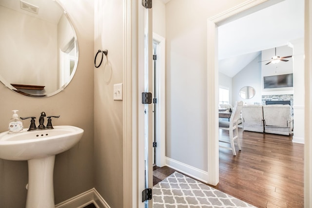 bathroom featuring baseboards, lofted ceiling, ceiling fan, wood finished floors, and a fireplace