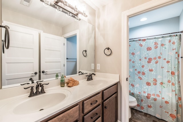 bathroom with toilet, double vanity, visible vents, and a sink