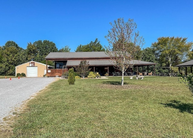 view of front of property with a front yard, gravel driveway, metal roof, and an outbuilding