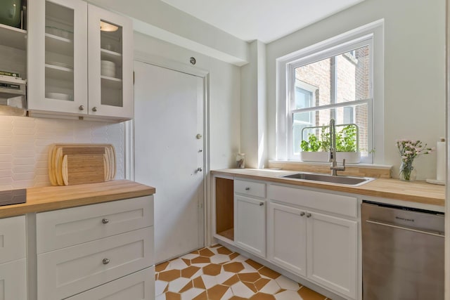 kitchen with light floors, stainless steel dishwasher, glass insert cabinets, a sink, and wood counters