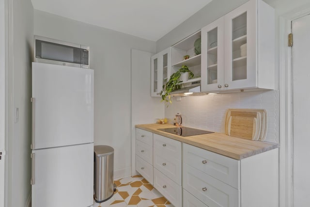 kitchen with stainless steel microwave, backsplash, glass insert cabinets, freestanding refrigerator, and white cabinets