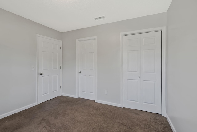 unfurnished bedroom featuring baseboards, visible vents, dark colored carpet, and a closet