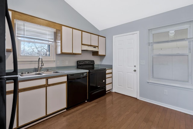 kitchen featuring dark wood-style floors, lofted ceiling, a sink, under cabinet range hood, and black appliances