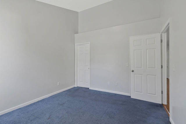 unfurnished bedroom featuring dark colored carpet, a towering ceiling, and baseboards