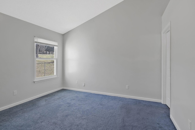 empty room with lofted ceiling, dark carpet, and baseboards