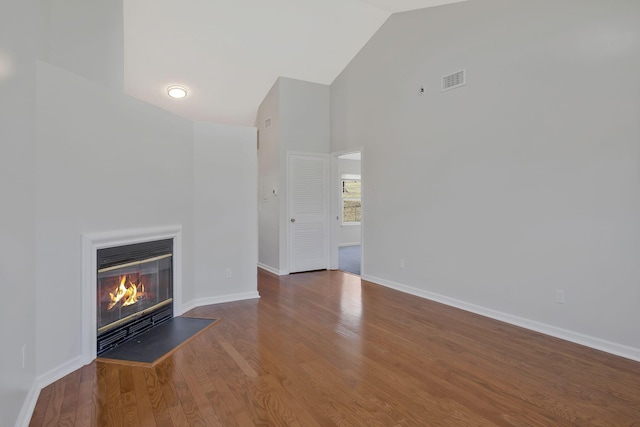 unfurnished living room with visible vents, a glass covered fireplace, wood finished floors, high vaulted ceiling, and baseboards