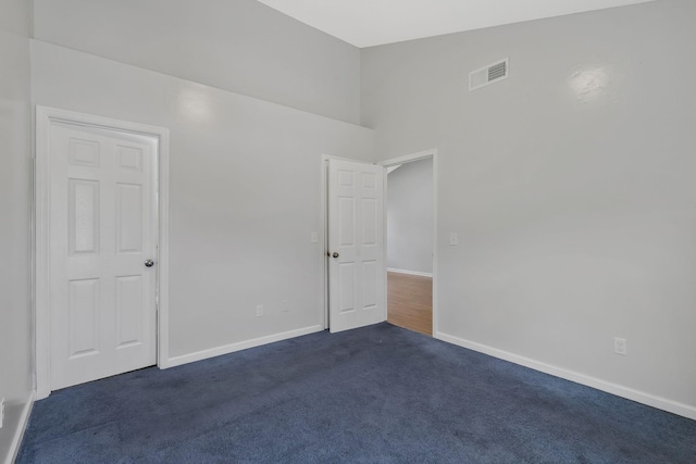 unfurnished room with high vaulted ceiling, dark carpet, visible vents, and baseboards