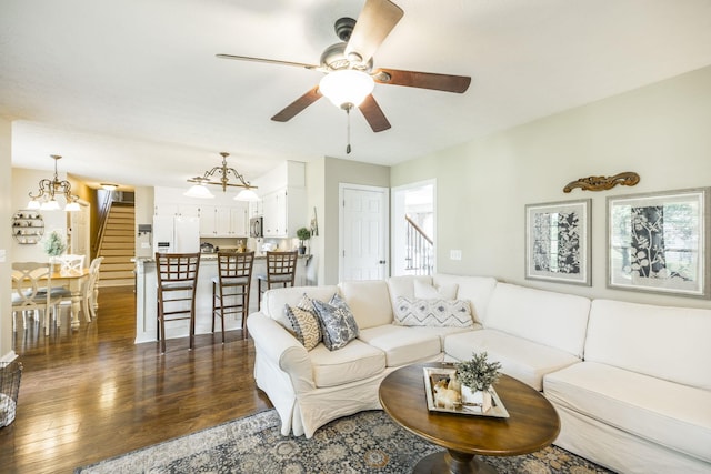 living room featuring dark wood-style floors, ceiling fan with notable chandelier, and stairs